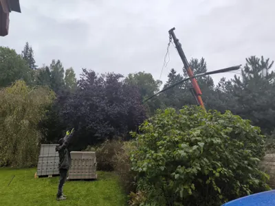 Hydraulická ruka podává tvárnice nad zahradu.